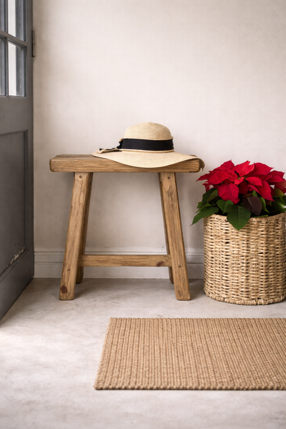 Wooden milk stool with a sun hat and potted plant against a neutral wall.